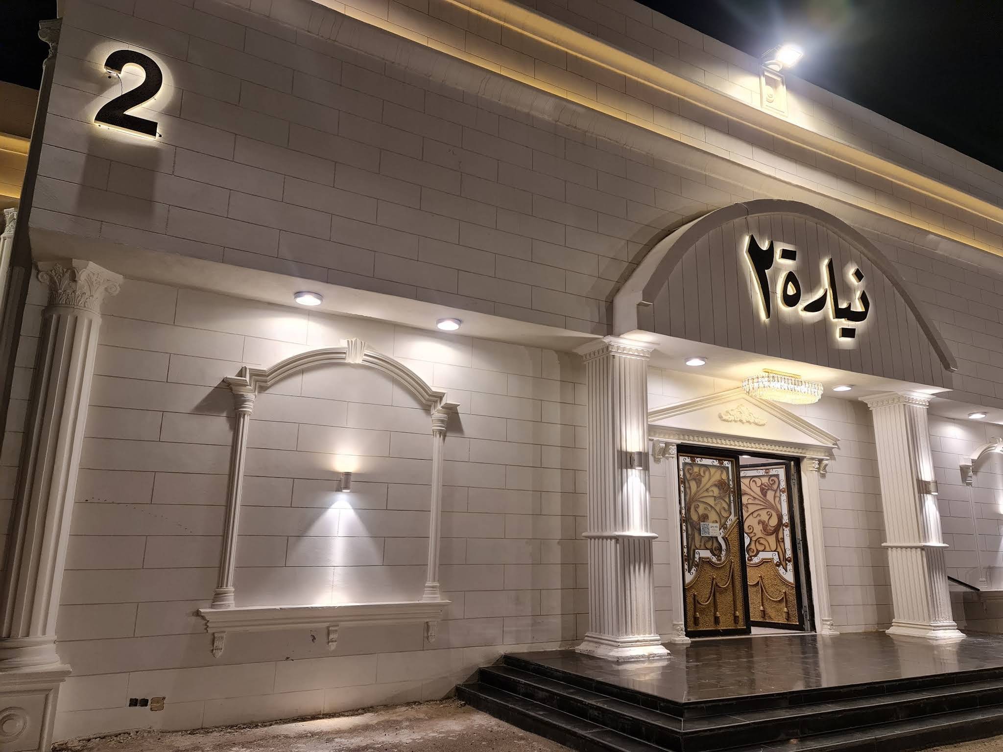 مدخل «نيارة ٢» بواجهة بيضاء وباب مزخرف وإضاءة ليلية