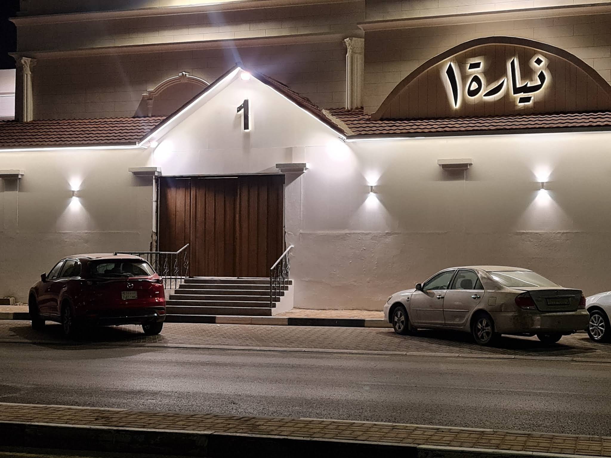 واجهة قاعة نيارة الأحساء ليلًا ومدخل «نيارة ١» والمواقف أمامها